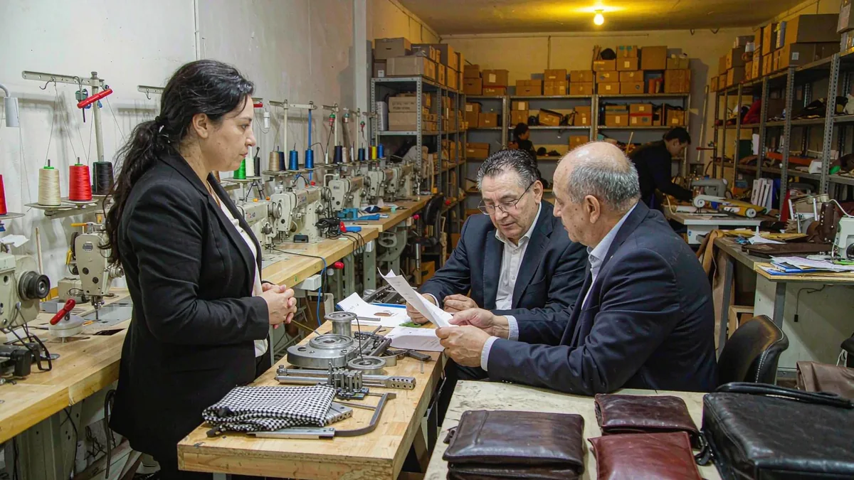 two people reviewing leather components and sample notes across a shared workbench